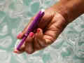 Dłoń z różowym lakierem trzyma fioletowy aplikator tamponu. Pokazano, jak zaaplikować tampon, trzymając go za sznurek.