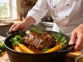 Un chef présente un rôti de veau en cocotte, savamment braisé avec des carottes et des herbes aromatiques.