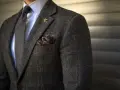 Elegancki mężczyzna w tweedowej marynarce, białej koszuli z kołnierzykiem kent, szarym krawacie i ozdobnej poszetce.