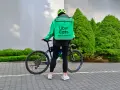 Dostawca Uber Eats w zielonej kurtce i kasku stoi obok roweru.