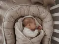 Śpiące dziecko w kokonie niemowlęcym z motywem gęsi. Czy warto zainwestować w taki kokon? Zapewnia poczucie bezpieczeństwa.