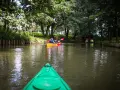 Dwie osoby płyną kajakiem po rzece, odkrywając malownicze radunia szlaki. Zielony kajak z przodu zaprasza do dalszej podróży.