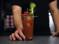 Bloody Mary na soku pomidorowym kontra na passacie. W szklance drink z lodem, ozdobiony oliwkami, suszonym pomidorem, kiełbaską i selerem.