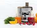 Une centrifugeuse ou extracteur prépare des jus frais avec des fruits et légumes. Ici, des jus d'orange, de carotte et de baies, avec des oranges, des carottes et des baies.