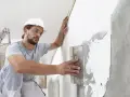 Artisan appliquant un enduit sur béton intérieur, préparant le mur pour une finition parfaite.