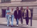 Fünf Freunde spazieren lässig, alle tragen Jeans. Welche Jeans sind in? Weite Schnitte und helle Waschungen dominieren den Look.