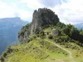 Pequeña ermita de piedra en la ruta de las ermitas, rodeada de vegetación y con imponentes montañas al fondo.
