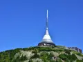 Wieża telewizyjna Ještěd, jedna z głównych libereckich atrakcji, góruje nad zielonym wzgórzem pod błękitnym niebem.