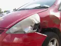 Uszkodzony czerwony samochód, zniszczony reflektor i wgniecione błotnik. Zastanawiasz się, ile kosztuje złomowanie auta po takim wypadku?