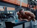 Man gör armhävningar på en bänk i gymmet, en shaker med blå dryck står bredvid. Detta är ett exempel på hur byggs muskler.