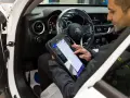 Meccanico usa tablet per diagnosticare la centralina auto. Il dispositivo mostra le opzioni di controllo e i dati del veicolo.