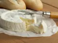 Un trozo cremoso de le camembert, con una rebanada cortada y lista para untar en pan crujiente.