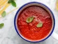 Sugo con pomodorini freschi, basilico e spaghetti crudi su marmo.