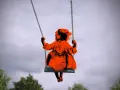 Ein orangefarbenes Kind schaukelt allein im Himmel. Es fühlt sich, als wäre ein Kind verloren.