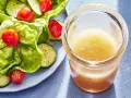 En burk med gyllene dressing till sallad står bredvid en fräsch sallad med sallad, gurka och tomater.