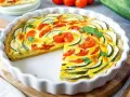 Eine köstliche Zucchini-Quiche mit Tomaten und frischer Petersilie, in einer weißen Quicheform serviert.