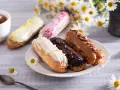 Eklery z czekoladą i profiteroles, ozdobione kwiatami, kuszą smakiem. Idealne na popołudniową herbatę.