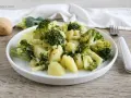 Un plato de brócoli con patatas, sencillo y saludable. Una patata entera y trozos de brócoli reposan cerca.