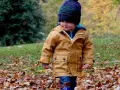 Mały chłopiec w jesiennej kurtce i czapce spaceruje po parku wśród opadłych liści. Idealne miejsce, gdzie na weekend z dzieckiem jesienią.