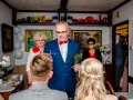 Mężczyzna w niebieskiej marynarce dokonuje tradycyjne błogosławieństwo, trzymając krzyż i gałązkę.