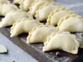 Surowe pierogi ułożone rzędami na drewnianej desce, posypane mąką.