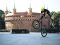 Kraków rowerem: kaskader na rowerze wykonuje akrobację przed Barbakanem.