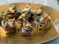 Deliciosos higos con foie sobre tostadas, adornados con pan de oro y tomillo, servidos en una bandeja dorada.