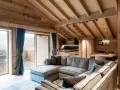 Cozy mountain chalet living room with sectional sofa, wooden beams, and large windows.