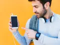 Mężczyzna w sportowym ubraniu pokazuje telefon, jak sparować zegarek z telefonem. Na nadgarstku ma smartwatch.