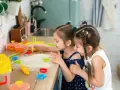 Dwie dziewczynki bawią się w kuchni, wycinając ciasteczka z ciasta. Radość i kreatywność w domowych zabawach.