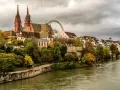 A scenic view of Basel's historic Minster and riverside buildings, perfect for a Basel itinerary. A Ferris wheel peeks out from behind the architecture.