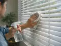 Hombre rocía limpiador y limpia persianas con paño. Guía práctica sobre como limpiar persianas para un hogar impecable.