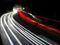 Voiture traversant un tunnel la nuit, capturant les traînées lumineuses des phares et des feux arrière grâce à des photos pose longue.