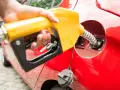 En hand håller en gul pump för att tanka en röd bil. Undrar du vad kostar diesel i Norge?