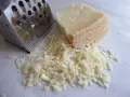 Tarty kawałek parmezanu i świeżo starty ser obok tarki. Dowiedz się, jak przechowywać parmezan, by zachował świeżość.