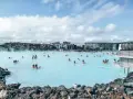 Ludzie kąpią się w turkusowej wodzie geotermalnej Blue Lagoon, otoczonej wulkanicznymi skałami i nowoczesnymi budynkami.