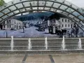 Ustroń rynek: fontanna i mural przedstawiający historyczne miasto z ludźmi w strojach z epoki i zabytkowymi samochodami.