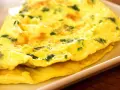 Złożony omlet z zielonymi ziołami na białym talerzu.
