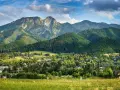 Widok na Giewont, majestatyczny szczyt o imponującej wysokości, otoczony zielonymi lasami i malowniczą wsią u podnóża.