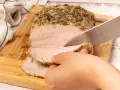 Un jugoso lomo a la sal, cubierto de hierbas, se corta en rodajas tiernas sobre una tabla de madera.