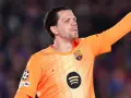 Wojciech Szczęsny w pomarańczowej koszulce bramkarskiej FC Barcelony, z podniesioną ręką, gotowy do obrony.