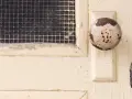 Maniglia usurata su porta interna tamburata, pronta per essere rinnovata. La rete della finestra è visibile.