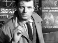 Młody Andrzej Maj, z palcem uniesionym w geście ostrzeżenia, stoi przed plakatem filmu "Werr Cruz" z Garym Cooperem.
