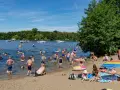 Menschen genießen das Reschensee baden an einem sonnigen Tag. Kinder planschen, Erwachsene schwimmen und entspannen am Ufer. Boote gleiten über das Wasser.