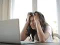 Zestresowana kobieta przy laptopie, szukająca informacji o odszkodowanie za nękanie przez firmę windykacyjną.