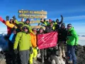 Glückliche Gruppe feiert auf dem Gipfel des Kilimandscharo. Sie haben den Gipfel erreicht und halten ein Banner hoch. Ein unvergessliches Erlebnis, den Kilimandscharo zu besteigen!