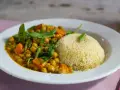 Un plato de cuscus con verduras, garbanzos y zanahoria en una salsa dorada, decorado con hojas verdes.