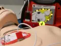 Defibrylator AED podłączony do manekina, gotowy do użycia.