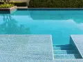 Élégante rénovation piscine mosaïque bleue, avec des marches carrelées et une végétation luxuriante.
