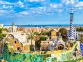 Kolorowe mozaiki i fantazyjne budowle Parku Güell, dzieło Antonio Gaudiego, na tle błękitnego nieba i Barcelony.